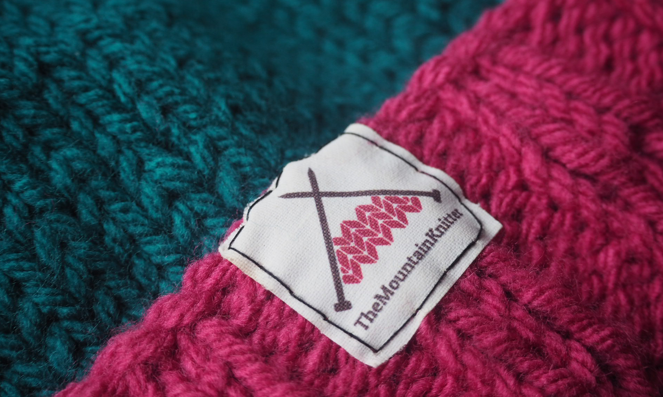 Close up photo of a hat label with the two-tone Mountain Knitter logo printed onto the label